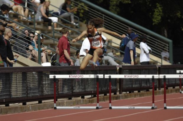 Athlete prepares for pole vault on a track with others watching.