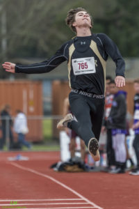 Athlete prepares for pole vault on a track with others watching.