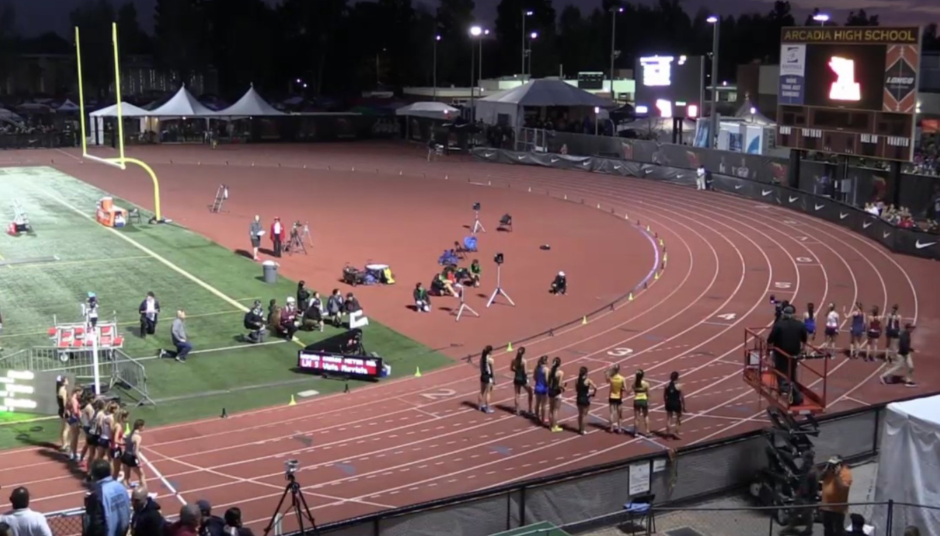 Athlete prepares for pole vault on a track with others watching.