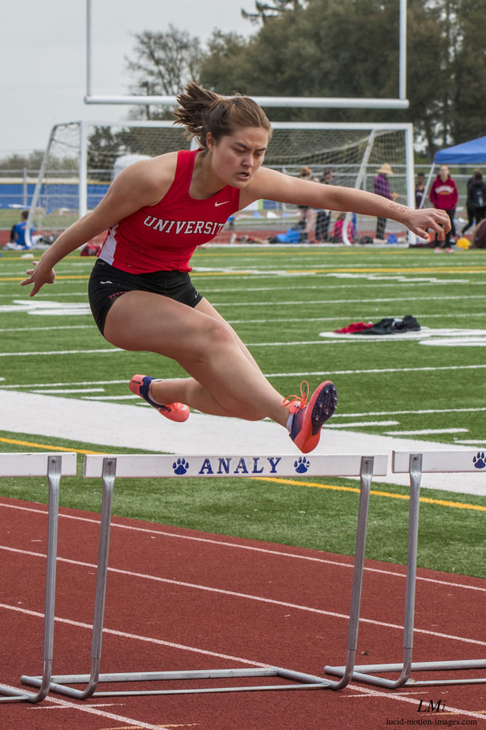 Athlete prepares for pole vault on a track with others watching.