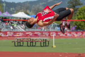 Athlete prepares for pole vault on a track with others watching.