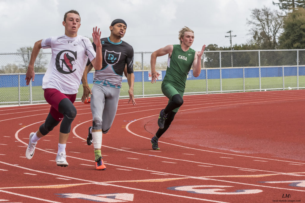 Athlete prepares for pole vault on a track with others watching.