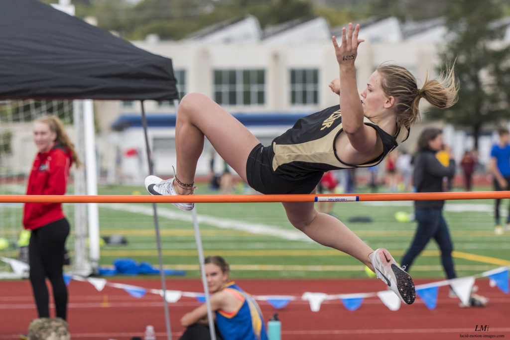 Athlete prepares for pole vault on a track with others watching.