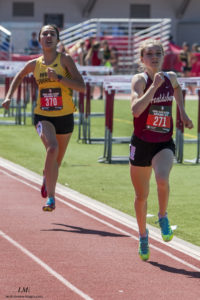 Athlete prepares for pole vault on a track with others watching.