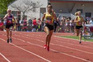 Athlete prepares for pole vault on a track with others watching.