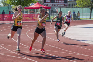 Athlete prepares for pole vault on a track with others watching.