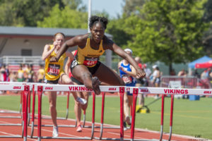 Athlete prepares for pole vault on a track with others watching.