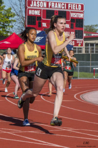 Athlete prepares for pole vault on a track with others watching.