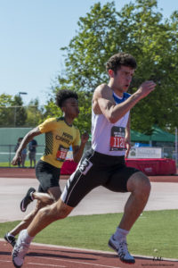 Athlete prepares for pole vault on a track with others watching.