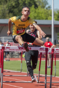 Athlete prepares for pole vault on a track with others watching.