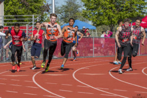 Athlete prepares for pole vault on a track with others watching.
