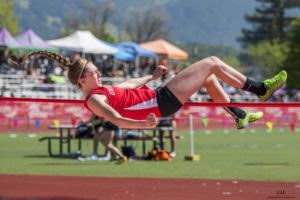 Athlete prepares for pole vault on a track with others watching.