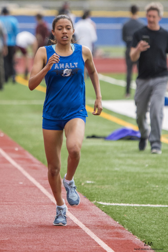 Athlete prepares for pole vault on a track with others watching.