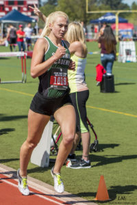 Athlete prepares for pole vault on a track with others watching.
