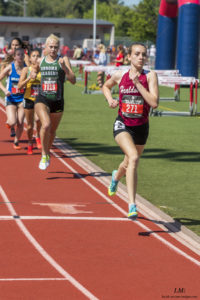 Athlete prepares for pole vault on a track with others watching.