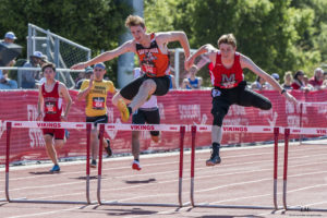 Athlete prepares for pole vault on a track with others watching.