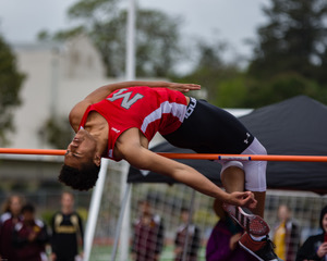 Athlete prepares for pole vault on a track with others watching.