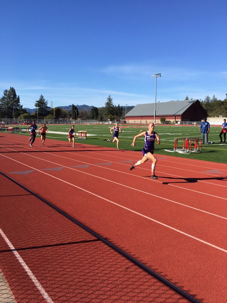 Athlete prepares for pole vault on a track with others watching.