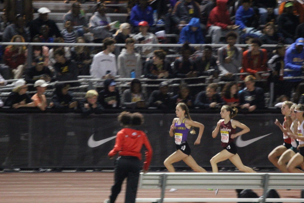 Athlete prepares for pole vault on a track with others watching.