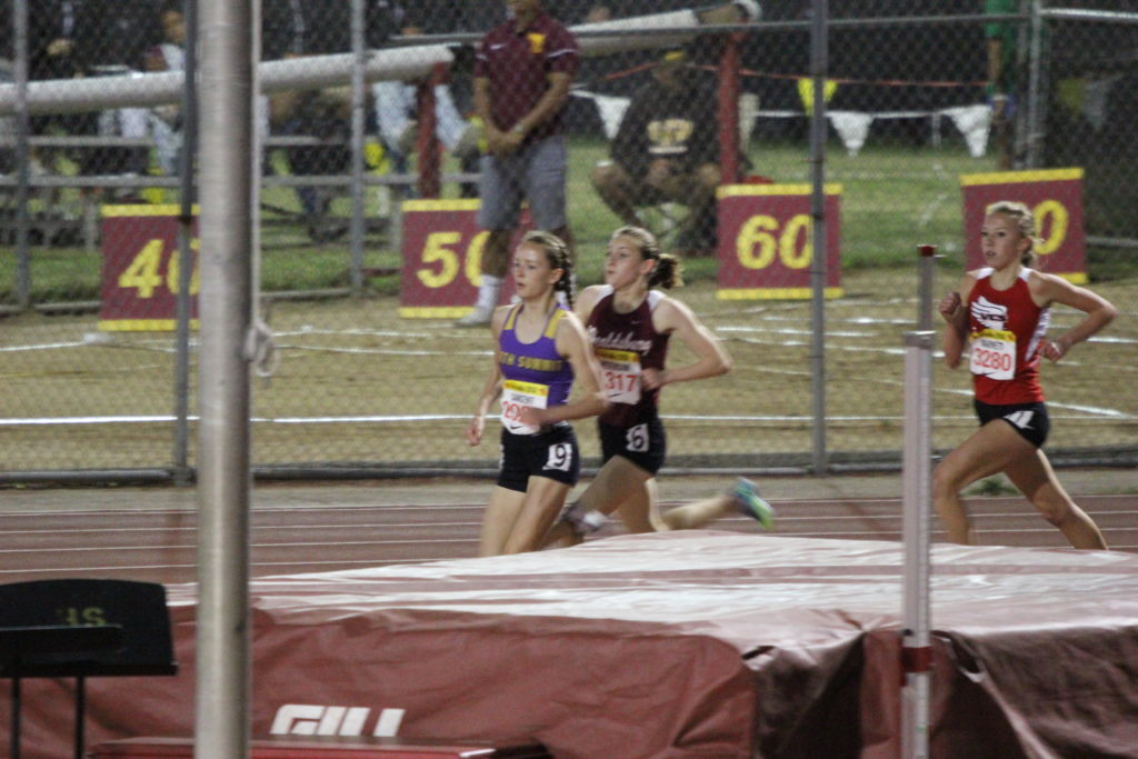 Athlete prepares for pole vault on a track with others watching.