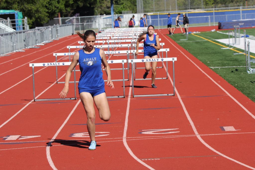 Athlete prepares for pole vault on a track with others watching.