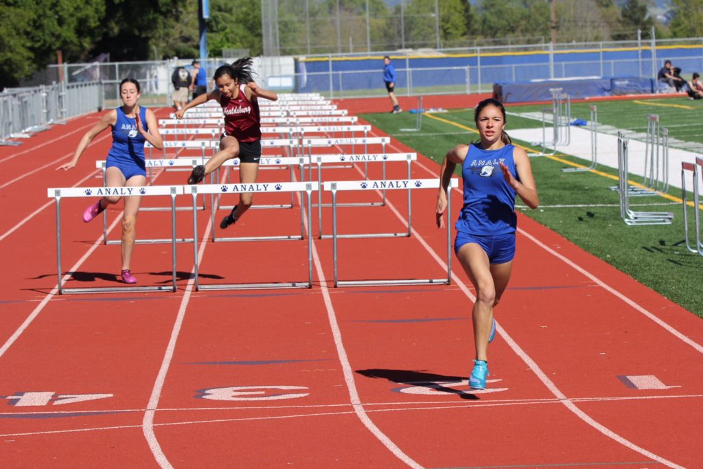 Athlete prepares for pole vault on a track with others watching.