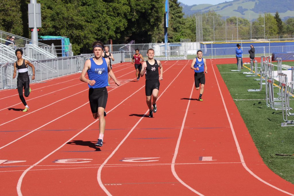 Athlete prepares for pole vault on a track with others watching.