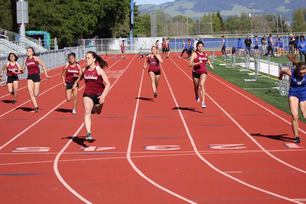 Athlete prepares for pole vault on a track with others watching.