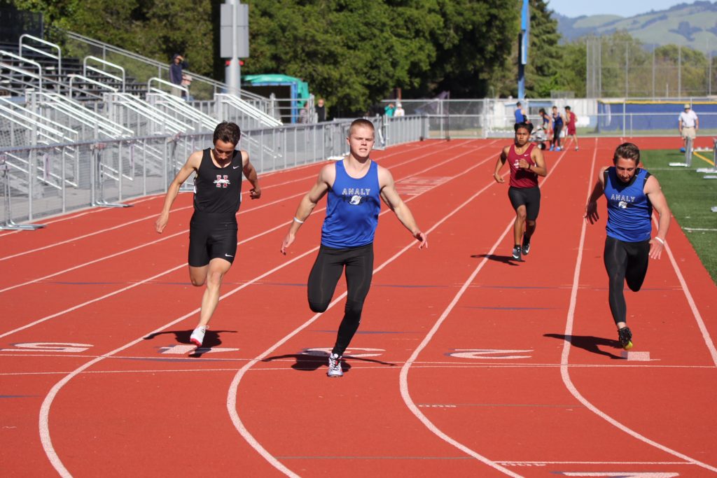 Athlete prepares for pole vault on a track with others watching.