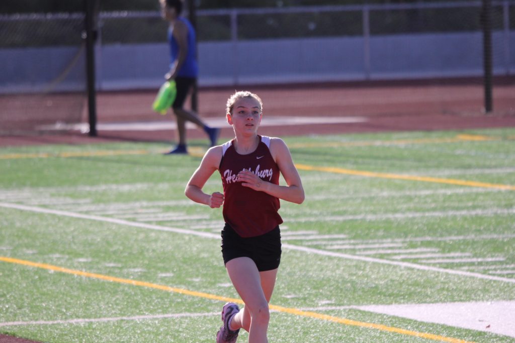Athlete prepares for pole vault on a track with others watching.