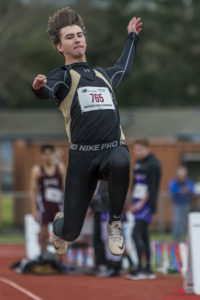Athlete prepares for pole vault on a track with others watching.