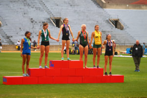 Athlete prepares for pole vault on a track with others watching.