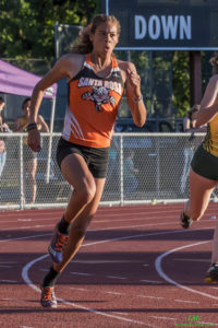 Athlete prepares for pole vault on a track with others watching.
