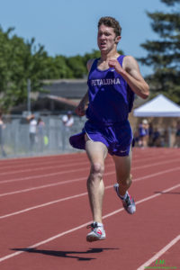 Athlete prepares for pole vault on a track with others watching.