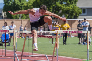 Athlete prepares for pole vault on a track with others watching.