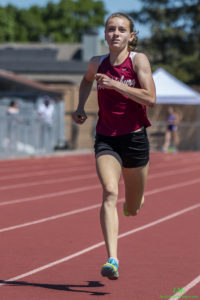Athlete prepares for pole vault on a track with others watching.