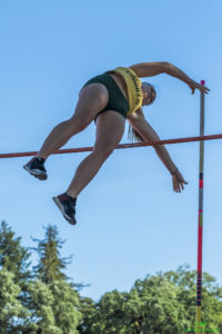 Athlete prepares for pole vault on a track with others watching.