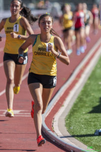 Athlete prepares for pole vault on a track with others watching.