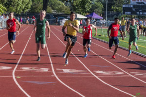 Athlete prepares for pole vault on a track with others watching.