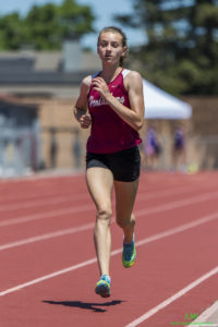 Athlete prepares for pole vault on a track with others watching.