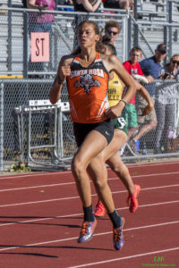 Athlete prepares for pole vault on a track with others watching.