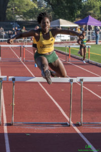 Athlete prepares for pole vault on a track with others watching.