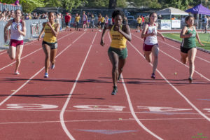 Athlete prepares for pole vault on a track with others watching.