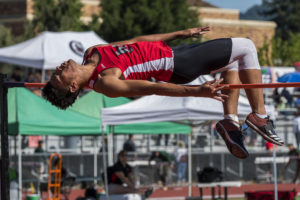 Athlete prepares for pole vault on a track with others watching.