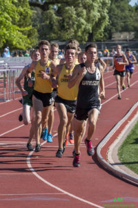 Athlete prepares for pole vault on a track with others watching.