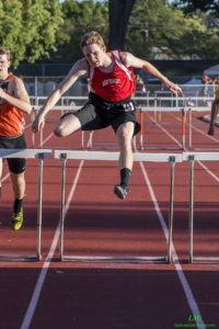 Athlete prepares for pole vault on a track with others watching.