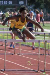 Athlete prepares for pole vault on a track with others watching.