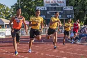 Athlete prepares for pole vault on a track with others watching.