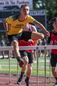 Athlete prepares for pole vault on a track with others watching.
