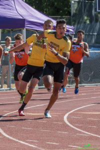 Athlete prepares for pole vault on a track with others watching.